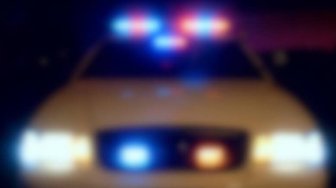 Blurred police car with flashing red and blue lights against a dark background; related to allegations of criminal activit...