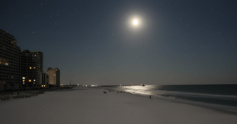 Gulf Shores beach scene: Buildings overlook a sandy shore with people enjoying the water, hinting at planning & zoning con...