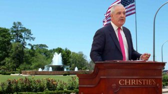 Man in suit speaks at podium near fountain; article discusses Fairhope land purchase concerns and city council decisions