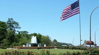 American flag waving above a civic center fountain and landscaped grounds, setting for the State of the City event