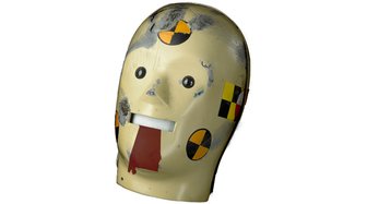 Abstract mask resembling a face, overlaid with black and yellow target markings, symbolizing legal scrutiny and ongoing mo...