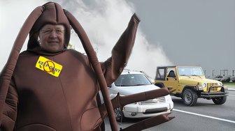 Man in a brown costume resembling a car, holding up a sign reading Keep Cant’t Out, referencing local political controversy